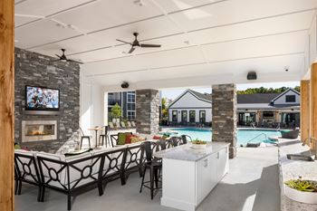 A modern outdoor kitchen with a stone fireplace and a television mounted on the wall.